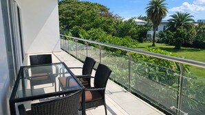 Un balcon doté d’une table et de chaises en verre, offrant une vue sur un jardin luxuriant et des palmiers.