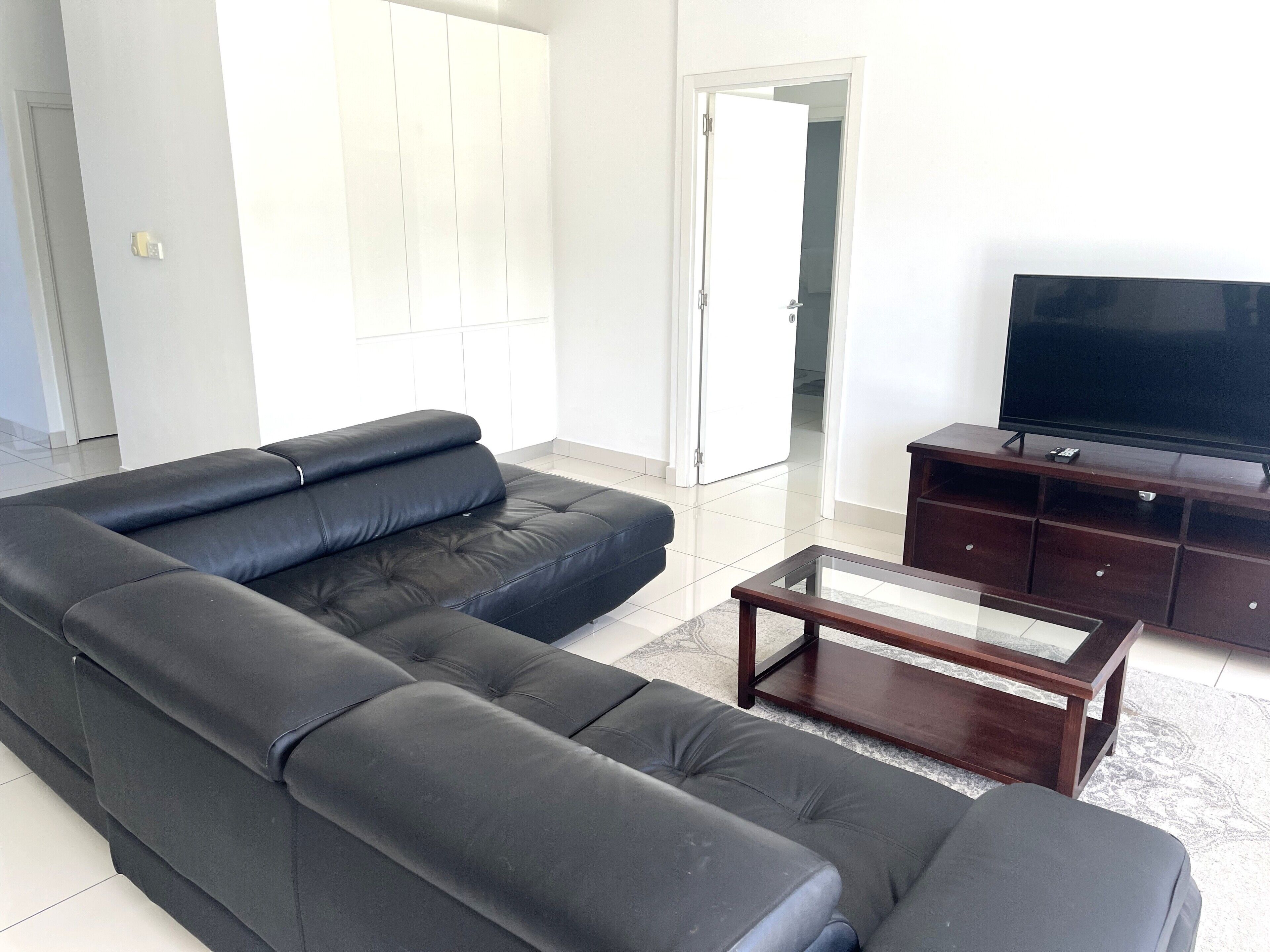 Una sala de estar con un sofá de cuero negro, una mesa de centro de madera y un televisor sobre un mueble de madera.