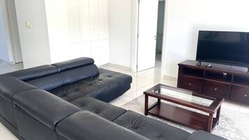 Una sala de estar con un sofá de cuero negro, una mesa de centro de madera y un televisor sobre un mueble de madera.