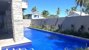 Une piscine bordée d’un mur en pierre, entourée de plantes tropicales et de palmiers.