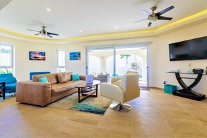 Ein geräumiges Wohnzimmer mit Sofa, Sessel, Couchtisch und Deckenventilator.