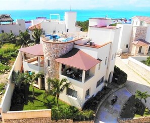 A modern multi-story building with a rooftop terrace, surrounded by greenery and a clear view of the sea. - Casa Elegante Luxury Villa (Isla Mujeres)
