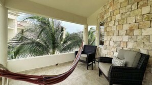 A balcony with a hammock, wicker furniture, and a stone wall. - Casa Elegante Luxury Villa (Isla Mujeres)