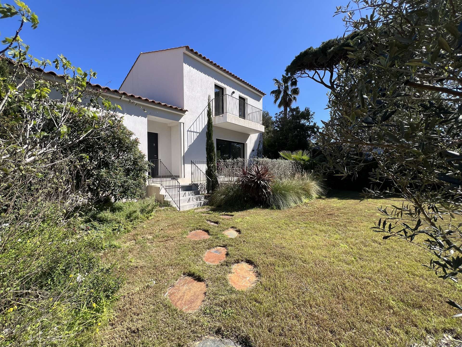 A two-story house with a balcony, surrounded by a garden with a stone pathway.