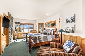 Une chambre à coucher avec un lit en bois, un canapé, une télévision et une fenêtre donnant sur des arbres.