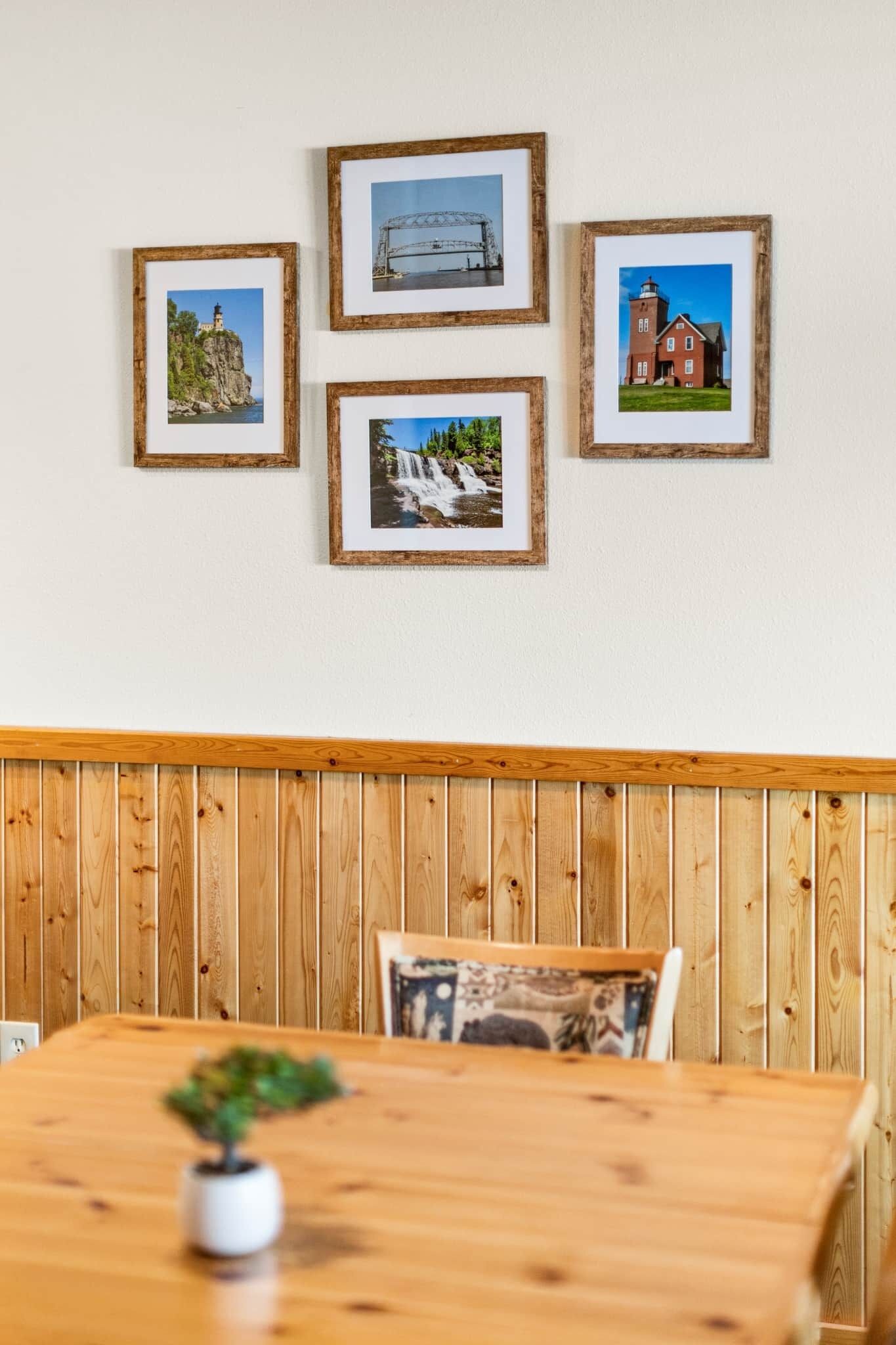 A dining area with a wooden table and bench, framed pictures on the wall, and a small potted plant.
