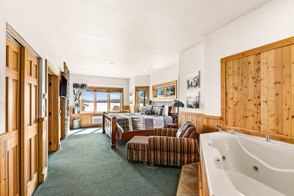 A bedroom with a large bed, a wooden wardrobe, a bathtub, and a view of the outdoors.