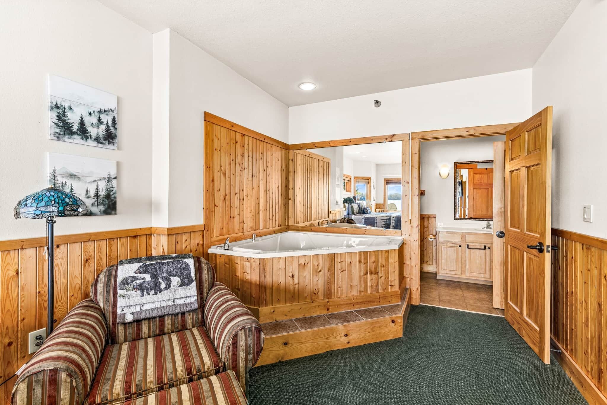 Une pièce avec une baignoire en bois, un canapé à rayures et un miroir qui reflète l’espace cuisine.