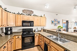 A kitchen with wooden cabinets, a black stove, a microwave, a coffee maker, and a sink.