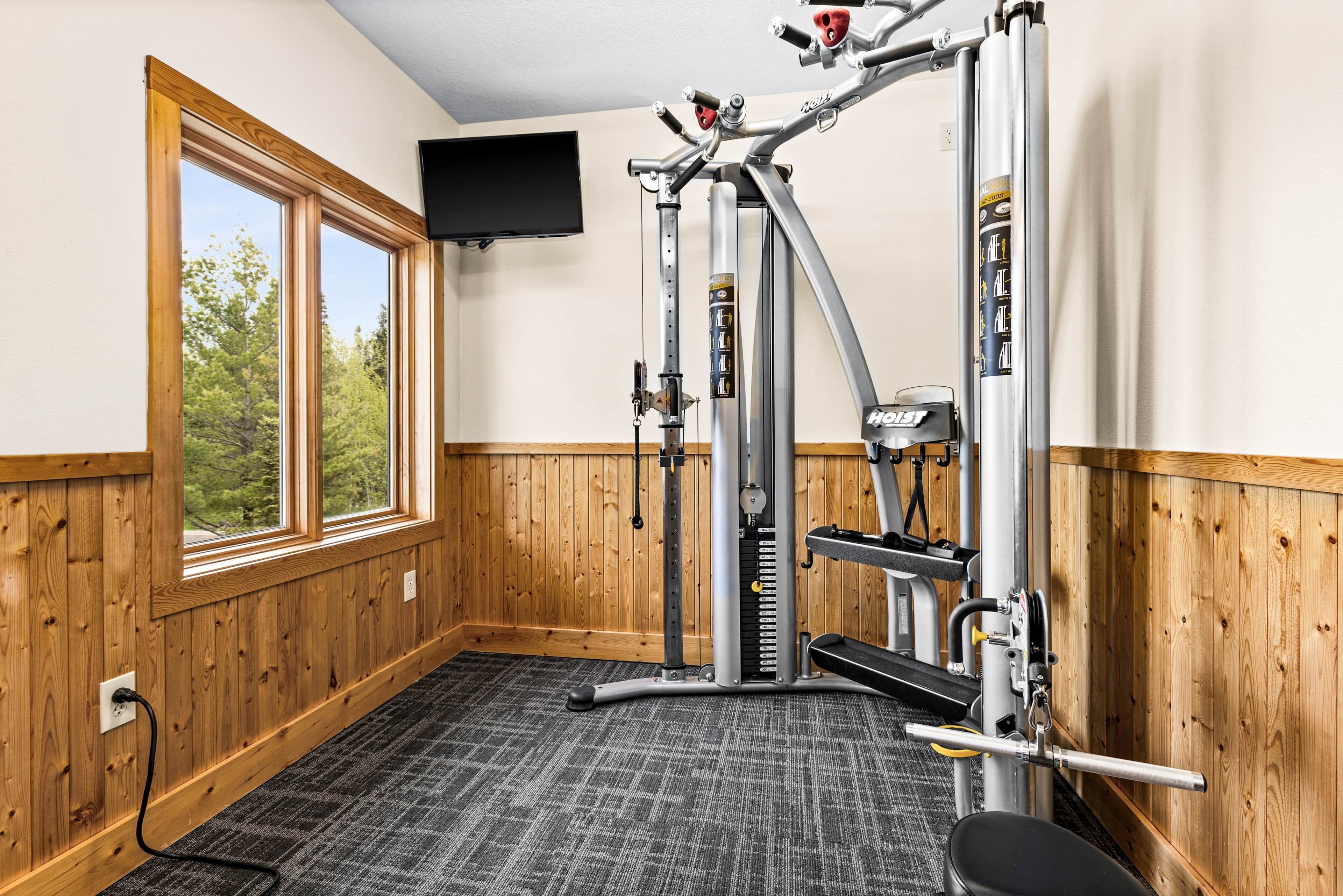 Ein Fitnessraum mit Klimmzugstange, Gewichtbank und an der Wand montiertem Fernseher.