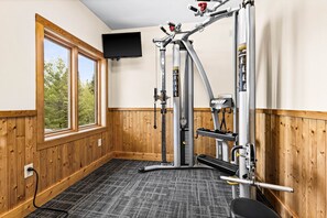 Een sportschool met een pull-up bar, een gewichtbank en een aan de muur bevestigde televisie.