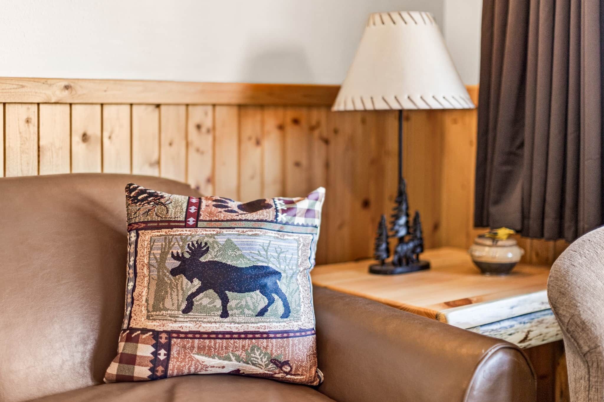Une pièce aux murs lambrés, avec un canapé en cuir marron, un coussin à motifs, une lampe et une petite table sur laquelle est posé un objet décoratif.