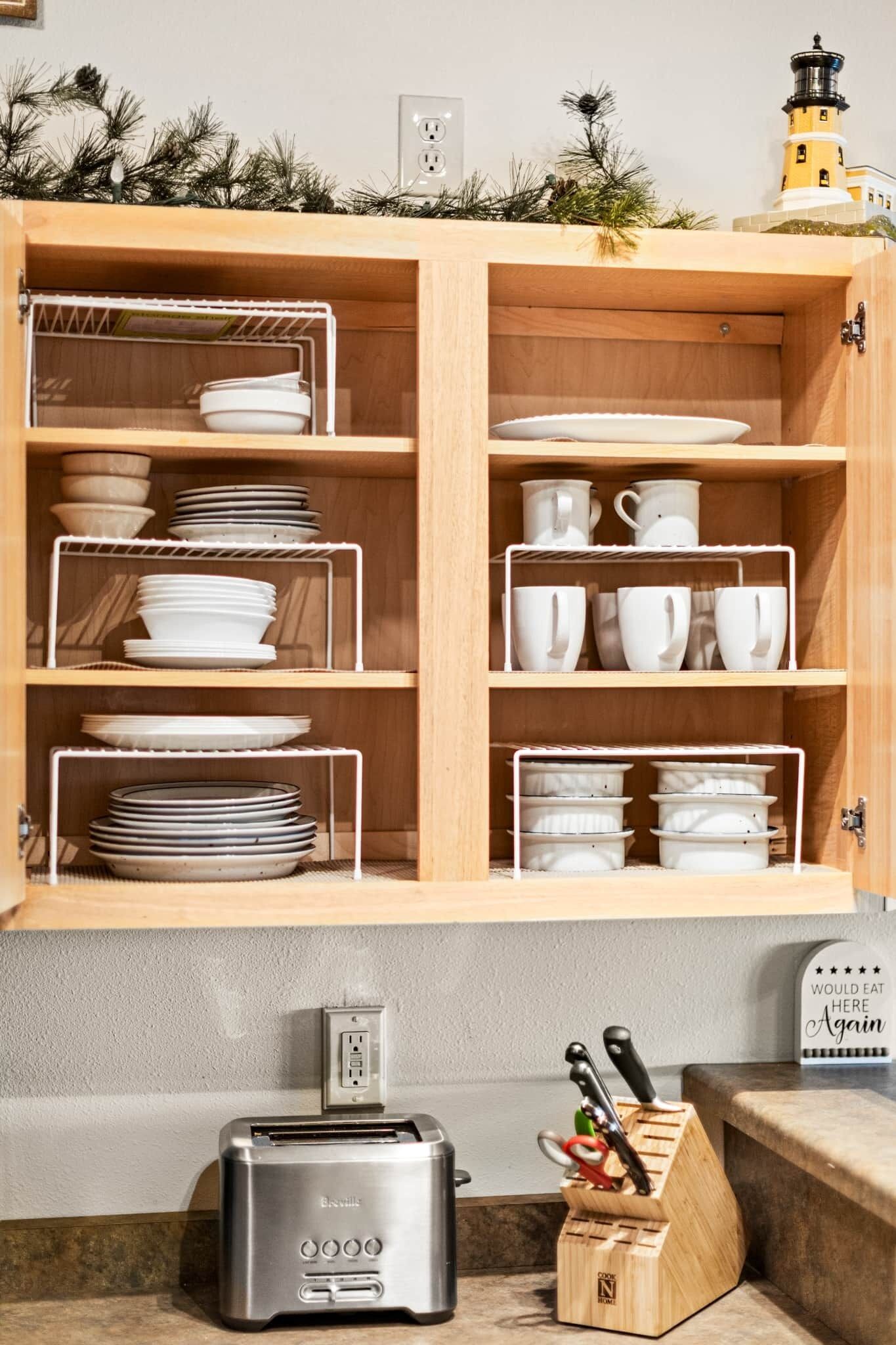 A kitchen with a wooden cabinet containing white dishes and cups, a toaster, and a knife block on the counter.