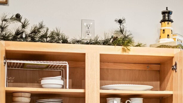 Une cuisine avec un meuble en bois contenant de la vaisselle et des tasses blanches, un grille-pain et un bloc à couteaux posé sur le plan de travail.
