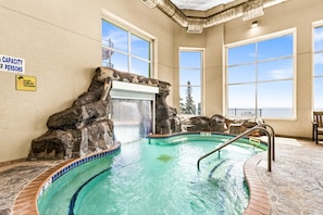Piscina interior con cascada, ventanas amplias y señal de aforo.