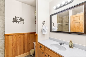 Un baño con tocador de madera, dos lavamanos, un espejo grande con iluminación y un adhesivo mural con paisaje de montaña.