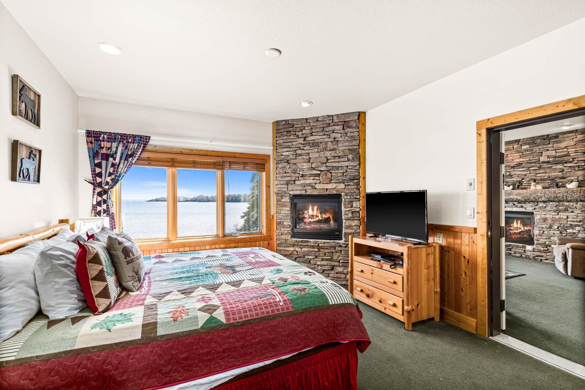 Une chambre avec un grand lit, une télévision, une cheminée et une vue sur un lac.