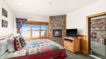 A bedroom with a large bed, a TV, a fireplace, and a view of a lake.