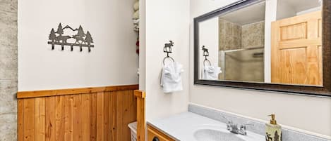 Ein Badezimmer mit einem hölzernen Waschtisch, zwei Waschbecken, einem großen, beleuchteten Spiegel und einer Wandsticker mit einer Berglandschaft.