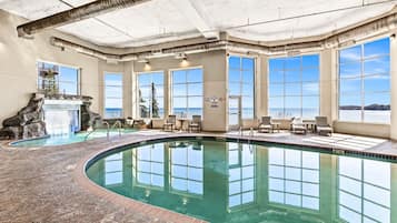 An indoor swimming pool with a waterfall feature, large windows, and a view of the sea.