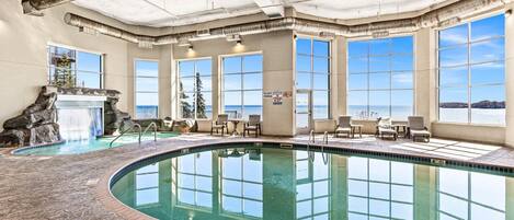 An indoor swimming pool with a waterfall feature, large windows, and a view of the sea.