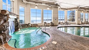 An indoor swimming pool with a stone wall, a waterfall feature, and multiple windows offering a view.