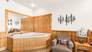 A wooden-paneled room with a large bathtub, a chair, and a small table with a lamp.