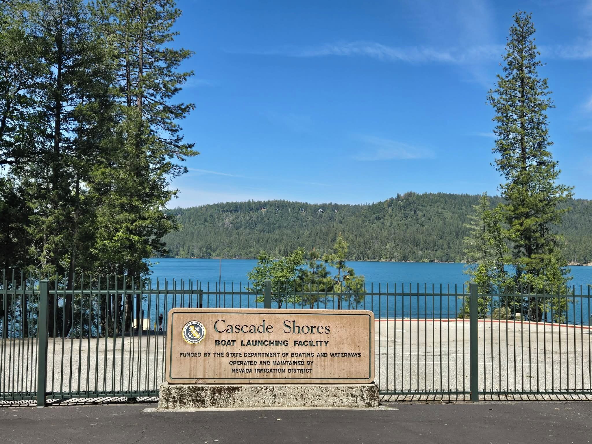Un panneau indiquant l’emplacement de la zone d’accès à l’eau pour les bateaux de Cascade Shores, avec une vue sur un lac et des collines boisées.