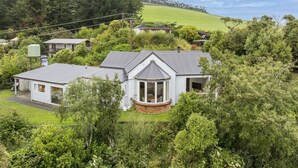 A residential house with a large garden, a conservatory, and a view of a hill. - Waitati Retreat - Coastal Calm Overlooking Blueskin Bay (Waitati)