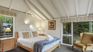 A bedroom with a bed, bedside tables, a chair, and a large window. - Waitati Retreat - Coastal Calm Overlooking Blueskin Bay (Waitati)