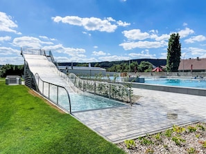 Uma piscina com um toboágua, rodeada por um gramado e céu claro.