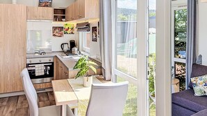 Une cuisine moderne avec des meubles en bois, une table à manger et des chaises. Une grande fenêtre offre une vue sur la verdure environnante.