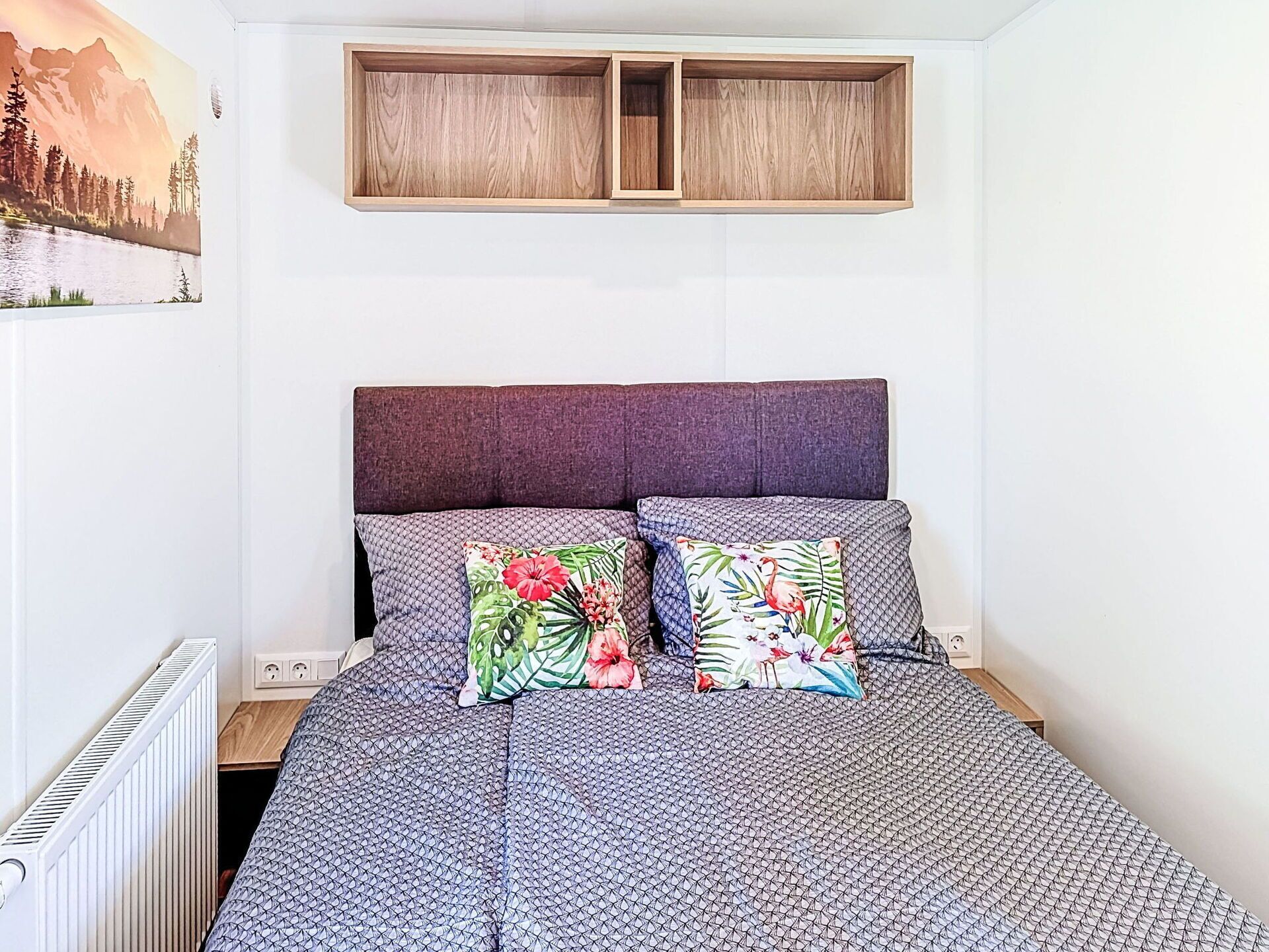 A bedroom with a bed, two pillows, a headboard, a wall-mounted shelf, and a painting.