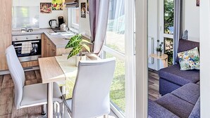 Une cuisine compacte dotée d’appareils électroménagers modernes, un coin repas avec une table et des chaises, et un canapé offrant une vue sur l’extérieur.