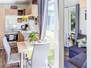 Een compacte keuken met moderne apparatuur, een eethoek met een tafel en stoelen, en een bank met uitzicht op het omliggende landschap.