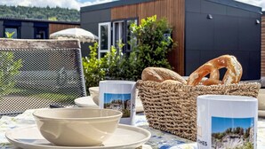 Un espace de restauration en plein air avec une table dressée pour deux personnes, un panier de pain et une vue sur un bâtiment moderne.