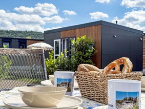 Een terras met eethoek, een tafel voor twee, een broodmand en uitzicht op een modern gebouw.