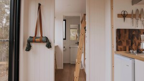 Un corridoio stretto con una scala a pioli, una borsa appesa e un angolo cottura con piano di lavoro in legno e coltelli.