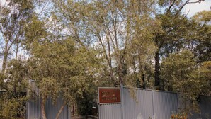 Un cancello metallico con un cartello che riporta la scritta 'WILDLIFE SANCTUARY' e un sentiero che si snoda attraverso un ambiente naturale, con alberi e arbusti.