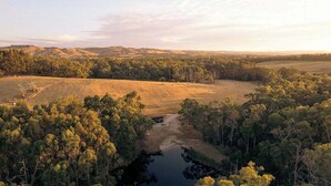 Un paysage rural avec une rivière, des arbres et des collines à l’horizon.