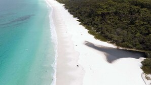 Luftaufnahme eines Strandes mit klarem türkisblauem Wasser, einem Sandstrand und einer dichten bewaldeten Küstenlinie.