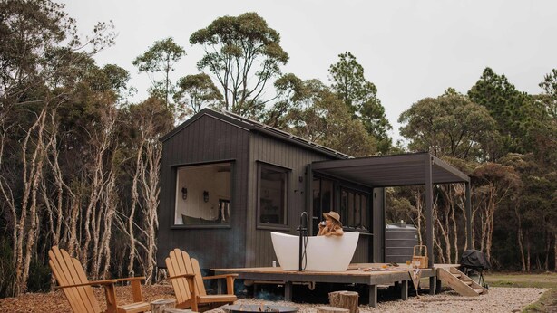 Eine Hütte mit einer großen Badewanne, Holzsesseln, einer Feuerstelle und einer Terrasse.
