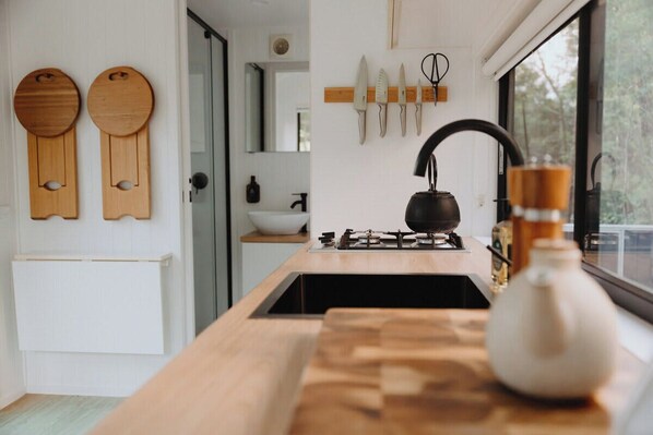 A modern kitchen with a wooden countertop, a gas stove, and a kettle. There are wooden wall decorations and a window with a view.