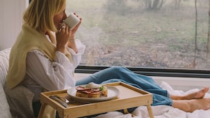 Eine Person sitzt am Fenster mit einem Tablett, das Essen und eine Tasse enthält.