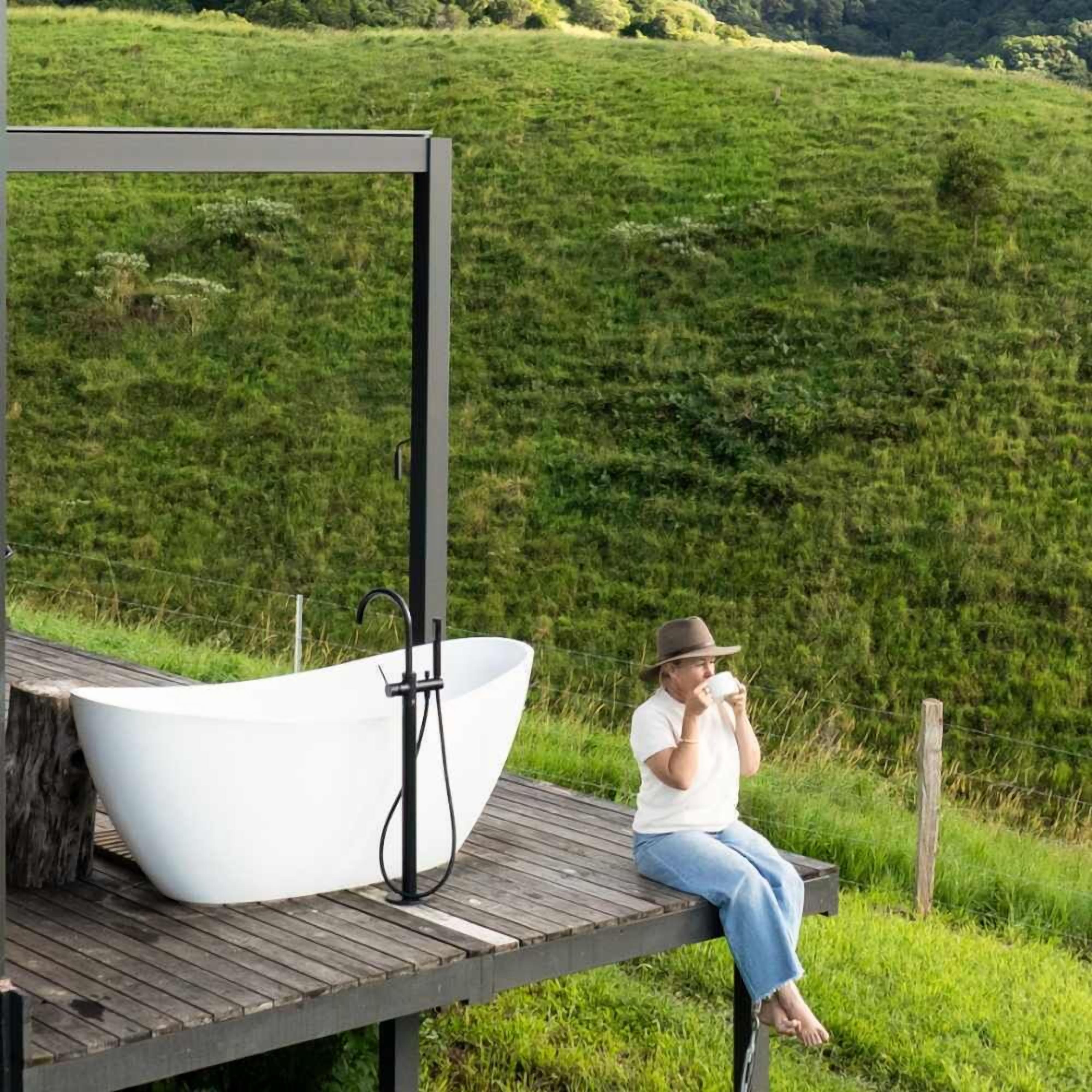 Eine Person sitzt auf einer Holzterrasse mit einer großen weißen Badewanne und einem schwarzen Ablaufrohr.