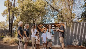 Um grupo de pessoas em frente a uma placa com a inscrição 'HILLS WILDLIFE SANCTUARY'.