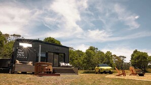 Een moderne camper met een zonnig interieur, zitplaatsen buiten en een geparkeerde auto.