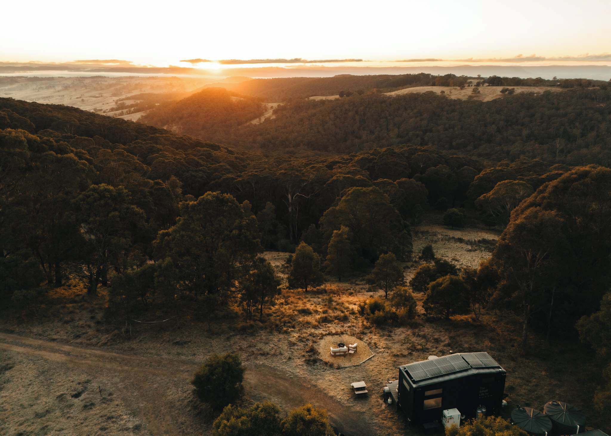 An aerial view of a campsite with a tent, a camper van, and a small building with solar panels.
