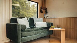 Een moderne woonkamer met een groene bank, een houten salontafel en een raam met uitzicht op bomen.