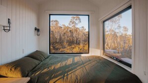 Une chambre avec un lit, une fenêtre donnant sur des arbres et un luminaire fixé au mur.
